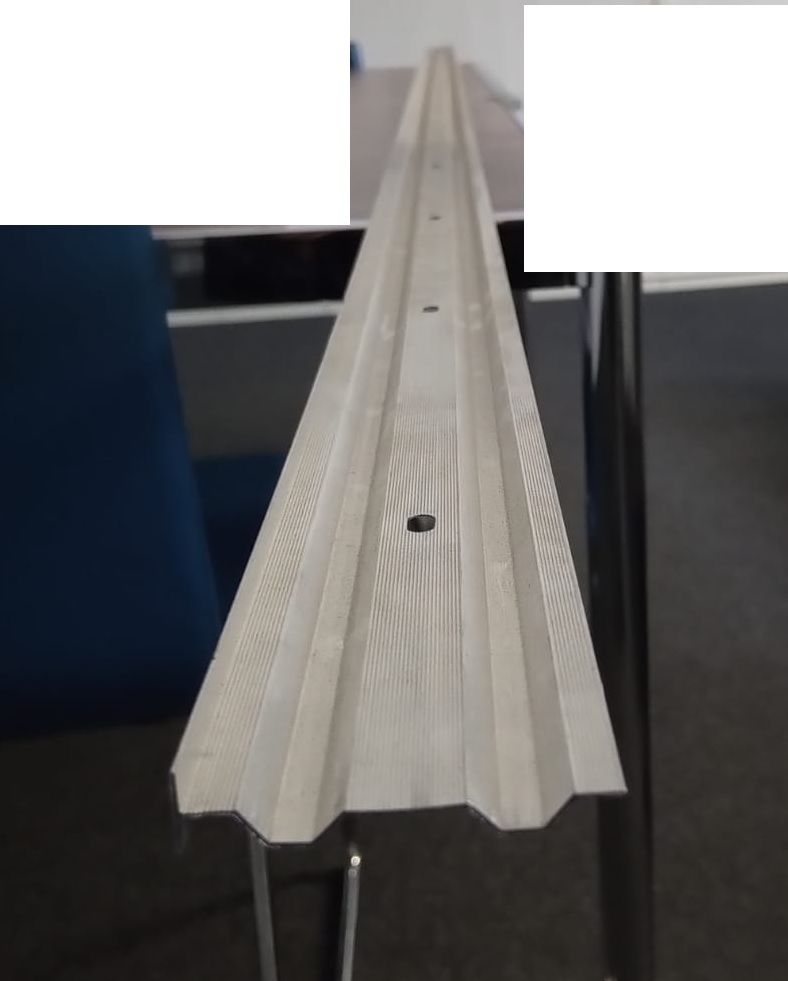 Varen er et aflangt emne af aluminium med to kantede buer i hele varens længde. Buerne ligger parallelle med samme afstand fra varens midte og sider. Midten og de to sider er flade i hele varens længde. Langs varens flade midte er der placeret aflange huller med ens afstand. Langs varens ene side er der en vinkelret kant, der både peger op og ned.
Det er oplyst, at varen anvendes til at klemme tagpap fast op ad en mur. De aflange huller i varen sikrer, at emnet kan bevæge sig i tagkonstruktionen, selv om det er skruet fast.
Efter det oplyste består varen af legeret aluminium.
Det fremgår af det modtagne materiale, at varen har følgende mål:
Bredde: 60 mm 
Længde: 3000 mm 
Tykkelse: 0,9 mm

Den vinkelrette kant er 12,5 mm høj.
