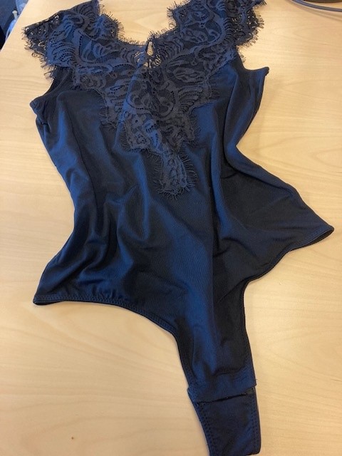 Varen er en ærmeløs bodystocking. Varen dækker overkroppen ned til skridtet. 

Varen har V-udskæring både for og bag. V-udskæringerne er forsynet med blondepåsætninger både for og bag.

Varens nederste del er udformet som en trusse og fremstår med høje benudskæringer som en såkaldt ”g-streng”.

Varen er fremstillet af glatstrikket trikotage med blondepåsætninger.

Varen har øget elasticitet i længderetningen men begrænset elasticitet i bredden.

Varen åbnes og lukkes i skridtet ved hjælp af tre forede trykknapper.
Varen dækker kroppen til skridtet og har en kropsnær pasform.
Varen er fremstillet af trikotagestof af polyamid og elasthan og er påsat blonder af polyamid.