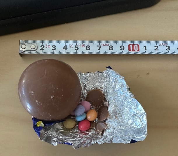 Varen er en brun og lidt flad kugleformet skal af mælkechokolade. Indeni chokoladeskallen ligger der farvede, sukkerovertrukne chokoladelinser. Varen smager sødt af mælkechokolade. 

Varen er indpakket i trykt metalfolie med snor til ophæng, så den ligner en flad julekugle.
Varen er en fødevare, der kan spises som den er.
Ifølge den medsendte ingrediensliste indeholder varen følgende:
Sukker, skummetmælkspulver, kakaosmør, kakaomasse, mælkefedt, emulgator, hvedemel, vallepulver, risstivelse og farvestoffer, aromastoffer og andre hjælpestoffer.
Varen foreligger i en detailsalgspapæske med 6 stk. 
Hver chokoladekugle har en angivet nettovægt på 18,5 g og måler ca. 5 cm i diameter og er ca. 2 cm høj.