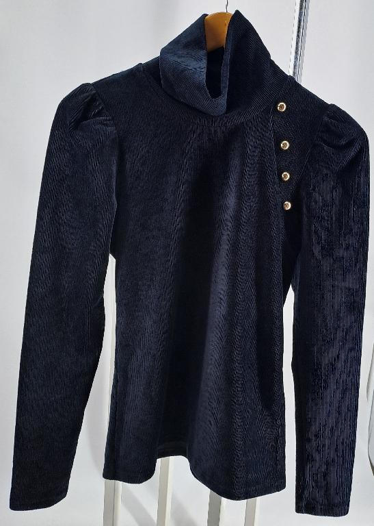 Varen er en tætsiddende langærmet pullover med rullekrave. Varen er fremstillet af ribbet fløjl af trikotage. Varen har en raglanlignende konstruktion ved venstre skulder i form af et lille skulderstykke, hvor der er 4 pynteknapper forrest på skulderstykket. Varen har påsatte pufærmer. Varen har ingen åbninger eller lukninger. 

Der er et ombuk med dobbeltsyning i ærmekanten og forneden.

Varen har elasticitet både lodret og vandret.
Varen er beregnet til at bliver båret direkte på overkroppen og har en tætsiddende pasform.
Varen består ifølge det oplyste af bomuld, polyester og elastan.
Varen findes i forskellige farver.