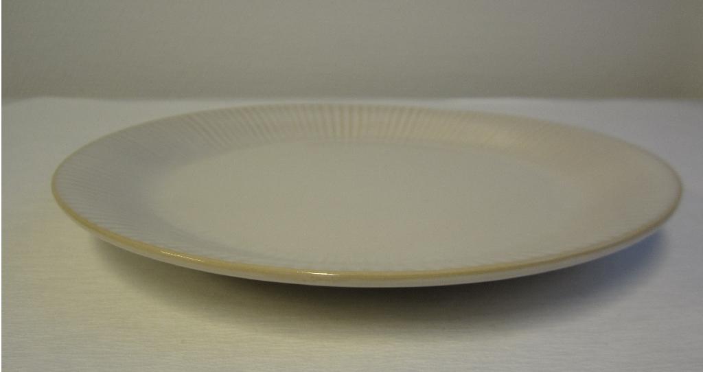 Varen er en rund, flad tallerken, med en ringformet forhøjning på undersiden. Fra denne forhøjning skråner kanten let opad, så kanten bliver let hævet. 
Overfladen er fuldt glaseret med en blank glasur, og varen fremstår glat med en let riflet struktur langs kanten. Forhøjningen på undersiden er ru og ikke glaseret.
Varen anvendes som bordservice.
Varen består af et keramisk materiale.
Det er oplyst, at varen foreligger med en diameter på 21 cm eller 27 cm.