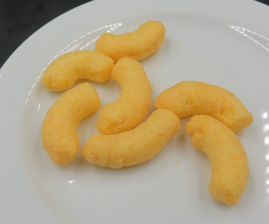 Varen er en tilberedt fødevare i form af aflange, buede snacks. Varen har en luftig, porøs og lidt sprød konsistens, med en saltet og krydret smag. Varen har en mild smag og duft af ost.
Varen er en fødevare klar til direkte fortæring.
Det er angivet på emballagen, at varen består af majsmel, helt hærdet raps- og kokosolie, ost, mælkepulver, salt, dextrose, vallepulver, solsikkeolie, aroma, løg, hvidløg, paprikaekstrakt, mælkeprotein og farve.
Varen foreligger i poser indeholdende 250 g.