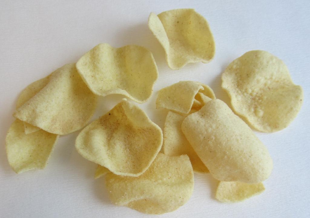 Varen er lysegule chips med en rund, ujævn form. På overfladen ses et lyst pulver med små røde bestanddele. Varen har en tør og sprød konsistens. 
Varen dufter lidt krydret og af olie og smager salt og lidt krydret.
Varen er en fødevare.
Det er oplyst, at varen består af kartoffelpulver, kartoffelstivelse, vegetabilske olier, salt, dekstrose, maltodekstrin, gærekstrakt, løg, vegetabilsk bouillon, surhedsregulerende middel, farvestof, tomat og krydderurt.
Det er oplyst, at varen er lavet af en dej, der er ekstruderet, tørret og fritteret.
Den fremsendte vareprøve er pakket i uigennemsigtig detailsalgsemballage indeholdende 140 gram.
