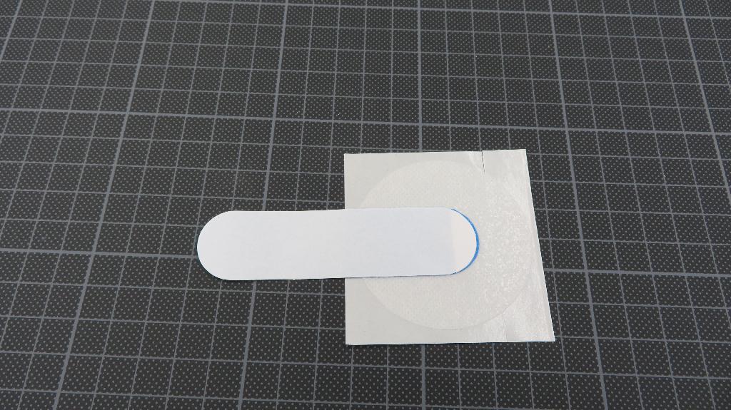 Varen er et fladt, rektangulært, blåt stykke plast der er fastgjort ca. midt på et stykke rundt fiberdug. 

Det blå stykke plast er 8,5 cm i længden og 2,2 cm bredt og afrundet i begge ender. På den ene side er et hvidt stykke aftageligt plast, som tjener som beskyttelse mod den selvklæbende side. 

Det runde fiberdugsstykke måler mellem 5,5 cm og 5,9 cm i diameter. På den ene side er et hvidt stykke aftageligt plast, som tjener som beskyttelse mod den selvklæbende side. Der er et hul i midten af fiberdugen med en diameter på 1 cm., hvorigennem man kan se det blå stykke plast, idet det overlapper hullet.
Det er oplyst, at varen anvendes til at fastholde og stabilisere EKG elektroder.
Varen består af plast, fiberdug og klæbemiddel.
Varen foreligger i poser med 50 stk., 500 stk. i bokse og 3000 stk. pr. kasse. 
Varen er pakket til detailsalg og har påsat en label, som bl.a. indeholder oplysninger om anvendelse, størrelse og holdbarhed.