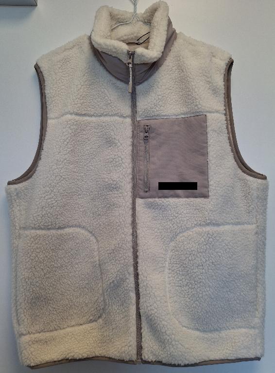 Varen er en vest af teddystof med gennemgående lynlås foran og en krave, så varen også kan dække halsen. Lynlåsen har ingen form for overlap, og varen går ned til hoften. Varen går lige op og ned og har ingen figursyninger, men snævrer en smule ind forneden. Langs sidesømmen er der i hver side en stor indstikslomme. På venstre side af varens forside er påsyet en lomme med lynlås. Lommen samt en del af kraven er lavet af et andet materiale end resten af varens yderside.
Langs ærmegab og varens underside er der påsyet et kantbånd.
På indersiden har varen et glat for, en inderlomme, en strop samt påsyede mærker med oplysninger om varens mærke, størrelse mv.
Varen er en beklædningsgenstand uden ærmer beregnet til at dække overkroppen.
Det er oplyst, at varen er fremstillet af 100 % polyester.
Varens yderside og kantbånd er fremstillet af trikotage, mens den påsyede lomme, en del af kraven samt foret er af vævet tekstil.
Den indsendte vareprøve er størrelse L.