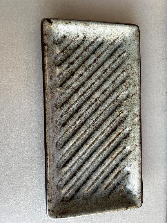 Varen er et rektangulært fad af glaseret keramisk materiale. Der er riller på skrå af varens flade del, men ikke op ad siderne. Under varens bund er der en smal, uglaseret, firkantet forhøjning.
Det er oplyst, at varen bl.a. kan bruges som sæbeskål eller bakke til at sætte ting på.
Varen er lavet af keramisk materiale.
Varen måler ca. 21 x 11 cm og er ca. 2 cm høj. Den fremsendte vareprøve er grå-brun og lidt grøn.