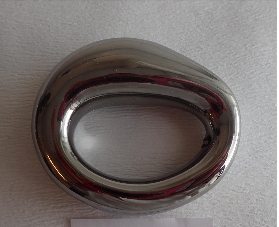 Varen er en ring med en uensartet oval form og ovalt hul i midten. Varens overflade er glat og skinnende og ligner metal.
Det er oplyst, at varen kan anvendes som en servietring.
Varen er af keramisk materiale, som efter det oplyste er overfladebehandlet for at opnå et metallisk udseende.
Varen måler ca. 6 x 7 cm og er ca. 2 cm høj på det tykkeste sted. Hullet i midten af varen måler ca. 3 x 5 cm.