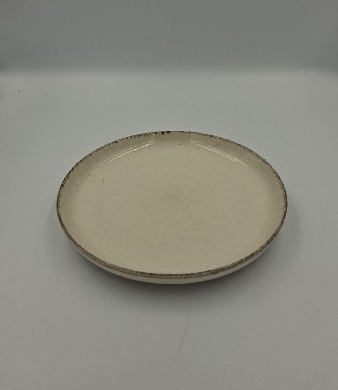 Varen er en rund tallerken med en kant der buer let opad. Varen er lavet af glaseret keramik.
Varen kan anvendes som bordservice.
Varen er af keramisk materiale.
Varen er beigefarvet med små brune prikker fordelt på hele overfladen. Langs den øvre kant, er der en smal og ujævn mørkebrun kant.
Varen er glaseret med en blank glasur på nær en ringformet forhøjning under bunden, som er uden glasur.

Det er oplyst, at varen måler 19 cm i diameter.