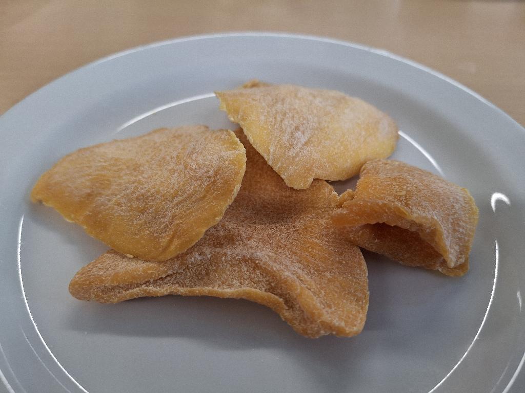 Varen er flade, uensartede stykker af tørret mango. Mangostykkerne er orange og har en ru overflade med lidt hvidt pulver. Varen har en sød og syrlig duft af mango og mild duft af ingefær. Varen smager sødt af mango og har en skarp ingefærsmag, der prikker på tungen.
Varen er en fødevare, der kan spises som den er.
Varen er tørret mango med ingefærsmag og består af mango, sukker, ingefærpulver, surhedsregulerende middel (citronsyre) og konserveringsmiddel (natriumdisulfit).
Varen foreligger i detailsalgspakninger med en nettovægt på 100 g.