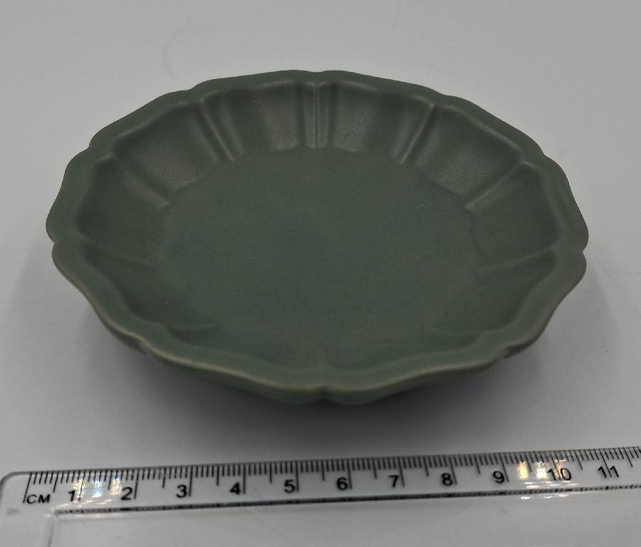 Varen er en lille glaseret keramikskål, der er formet som en blomst. Bunden er helt flad, mens kanten fremstår som blomsterblade, der buer lidt ud af, så varen får form som en skål. Kanten er dannet af 10 blomsterblade. Under varens bund er der en smal, uglaseret, ringformet forhøjning.
Det er oplyst, at varen er en sæbeskål og skal bruges til bloksæbe.
Varen er lavet af keramisk materiale.