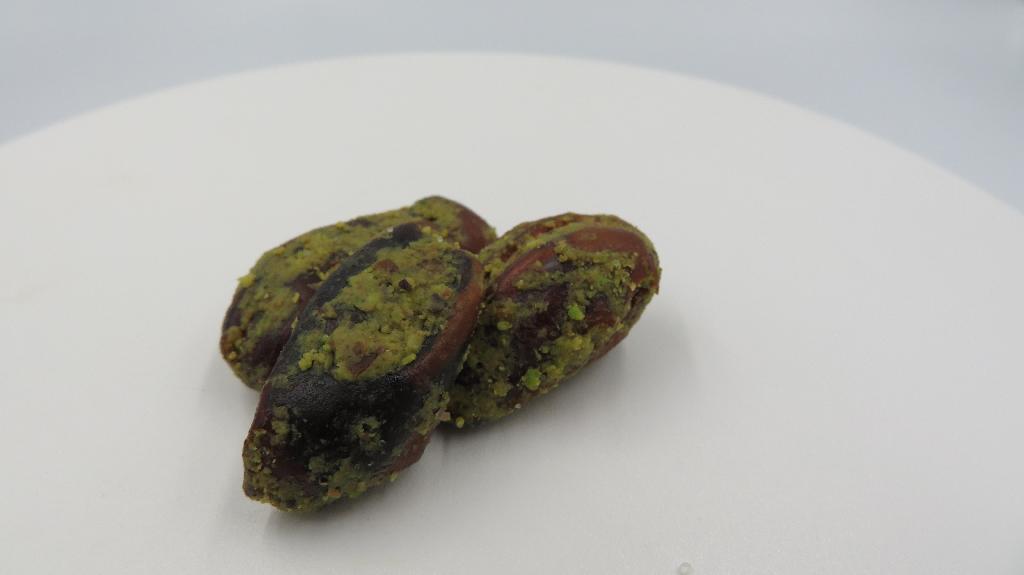 Varen består af tørrede dadler med en grøn masse, der danner en belægning på overfladen. Varen er lidt sej i konsistensen og dufter sødt. Smagen er sød og salt.
Varen kan indtages direkte som snack.
Ifølge ingredienslisten på emballagen indeholder varen udstenede dadler, pistacienødder, kokosolie og salt.
Den modtagne vareprøve foreligger i detailsalgsemballage indeholdende 100 g nettovægt.
