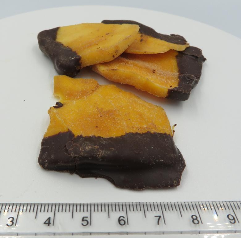 Varen er orangegule, aflange skiver af tørret frugt, som i den ene ende er dækket af et tykt lag chokolade. Skiverne har varierende størrelser og tykkelser, og der ses lidt hvidt pulver på varen, hvor den ikke er dækket af chokolade. Varen dufter sødt af chokolade og lidt af mango, mens den smager af mango og mørk chokolade.
Varen er en fødevare, der kan spises uden tilberedning.
Det er oplyst, at varen består af mango, mørk chokolade, emulgator, vaniljearoma, sukker, antioxidant og konserveringsmiddel.
Varen er pakket til detailsalg i folieposer med stå-bund, genluk i toppen og en nettovægt på 100 gram.