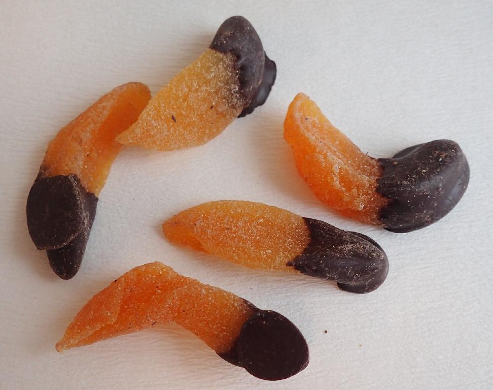 Varen er orange, aflange stykker af tørret frugt, som i den ene ende er dækket af et tykt lag chokolade. Stykkerne har varierende størrelser og tykkelser, og der ses lidt hvidt pulver på varen, hvor den ikke er dækket af chokolade. Varen dufter af chokolade og mildt af sød frugt, mens den smager sødt af fersken og mørk chokolade.
Varen er en fødevare, der kan spises uden tilberedning.
Det er oplyst, at varen består af fersken, mørk chokolade, emulgator, vaniljearoma, sukker, antioxidant, ferskenpulver og konserveringsmiddel.
Varen er pakket til detailsalg i folieposer med stå-bund, genluk i toppen og en nettovægt på 100 gram.