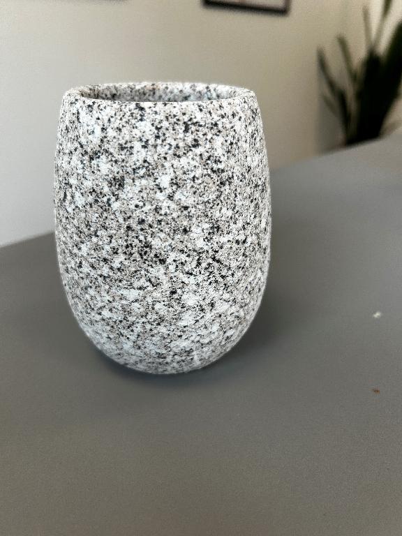 Varen er et krus med buede sider uden hank. Varen er ikke glaseret, men har en ru grå, hvid og sort overflade, som ligner granit.
Det er oplyst, at varen er en tandbørsteholder.
Varen er lavet af keramisk materiale.
Varen måler ca. 11 cm i højden, ca. 9 cm i største diameter, ca. 6,7 cm i diameter i toppen og ca. 5,9 cm i diameter i bunden.