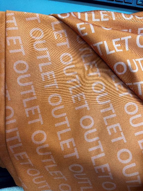 Varen foreligger som et rektangulært banner af tekstil, som er farvet orange på forsiden. Teksten ”OUTLET” fremgår både med store hvide bogstaver øverst på banneret og som en del af baggrunden, hvor teksten gentages igen og igen, er diagonal og bliver mindre tydeligt jo længere ned af banneret man ser. 
Hver ende af varen er foldet og syet så der dannes en tunnel i tekstilet.
Varen anvendes til ophængning for at reklamere for en bestemt tilbudskampagne
Varen består iht. det oplyste af 100 procent polyester
Det er oplyst at varen måler 1225x2550 mm, og er orange på forsiden med hvid tekst.