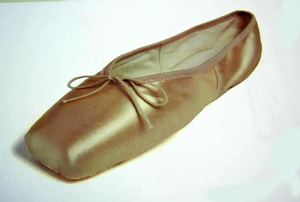 Zapatilla de baile. Zapatilla ligera, cerrada por detrás, cubriendo el talón. Parte superior de materia textil (satén) y suela de piel. Presenta un dobladillo hecho con una tira de materia textil en todo el borde superior de la zapatilla para sujetar el cordón que sirve para cerrar la zapatilla en torno al pie.