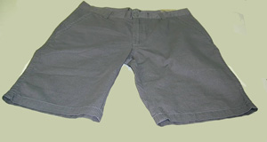 Pantalón corto de hombre de color gris con motas negras hecho con tejido de trama y urdimbre de algodón 100%. Cubre la parte inferior del cuerpo desde la cintura, envolviendo cada pierna por separado hasta por debajo de las rodillas. Presenta abertura delantera, cerrada de izquierda sobre derecha, mediante cremallera y botón. 

Lleva cinco bolsillos, dos delanteros y tres traseros. Las diferentes piezas de la prenda van unidas mediante costura con hilo.