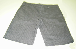 Pantalón corto de mujer de color gris hecho con tejido de trama y urdimbre de algodón (100%). Cubre la parte inferior del cuerpo desde la cintura, envolviendo cada pierna por separado hasta cubrir las rodillas. Presenta abertura delantera, cerrada de izquierda sobre derecha, mediante cremallera y botón, pero el corte de la prenda indica manifiestamente que ha sido concebida para mujer. 

Lleva cuatro bolsillos, dos delanteros y dos traseros. Las diferentes piezas de la prenda van unidas mediante costura con hilo.