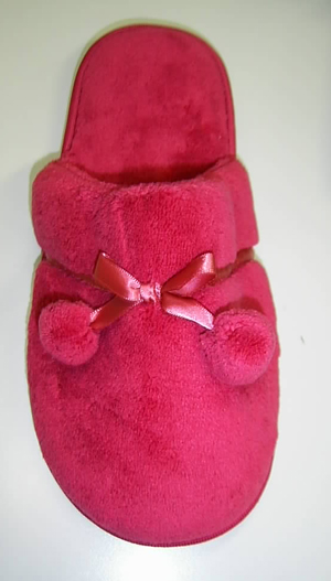 Calzado de casa. Zapatilla que deja el talón al aire, cubriendo casi todo el empeine. Parte superior de materia textil de color rojo (poliéster 100%), con una cinta y dos bolitas de adorno y suela constituida por una plancha de plástico, que en su parte exterior, en contacto con el suelo, lleva un tejido de punto muy fino de fibras de poliéster (90%) y algodón (10%) que está incrustado en la plancha plástica de la suela. Tanto el tejido de punto como el material plástico están en contacto con el suelo.