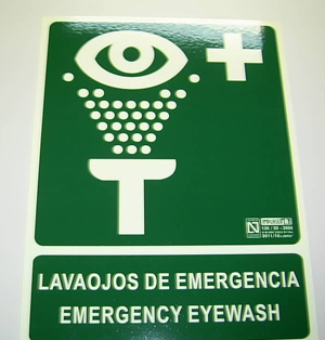 Placa de aluminio rectangular con unas medidas de 224 X 297 X 1 mm. En la cara principal lleva un dibujo y un texto ("lavaojos de emergencia/emergency eyewash") realizados con  pigmentos luminiscentes, al igual que los bordes, y el resto está pintada con tinta de color verde. Se utiliza para la señalización.