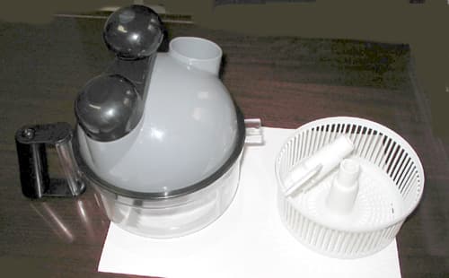 Aparato mecánico de plástico, accionado a mano, para preparar alimentos. Está constituído por un recipiente redondo y una tapa en forma de casquete en la que van incorporados los mecanismos, el manubrio y el eje que mueve los accesorios. Se presenta con cuchillas para picar, con un pequeño brazo para amasar y un cestillo para escurrir. Tiene un peso aproximado de 520 gr
