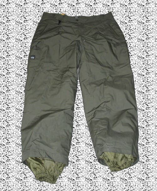 Pantalón largo de tejido de trama y urdimbre, fabricado en fibras sintéticas (nailon) laminado con recubrimiento de teflón, el forro interior es un forro polar hasta la rodilla, es también de nailon, la parte frontal, trasera y tobillos llevan refuerzos antidesgarros, lleva un cinturón y cinco bolsillos, los laterales y traseros con cierre de cremallera y lateral bajo con corchetes.