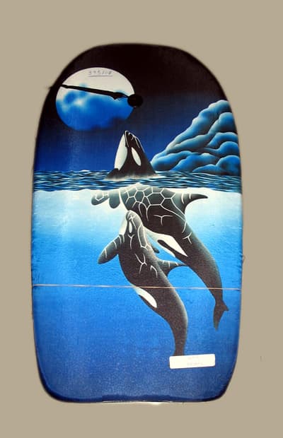 Artículo liso para la practica de deportes acuáticos, tipo tabla de surf, con unas dimensiones aproximadas de 84 cm. de largo, 46 cm. de ancho y 4 cm. de grosor. Está elaborado con plástico forrado de materias textiles y presenta en su cara superior una correa de materia textil para sujetarla al tobillo con un sistema de enganche tipo velcro.