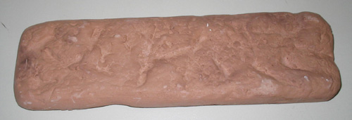 Placa fabricada con yeso moldeado y teñido con óxido de hierro. Tiene forma rectangular con unas medidas aproximadas de 19 x 5,6 x 1,2 cm. La cara interior es lisa y homogénea y la exterior imita la piedra sin pulir. Se presenta para su venta al por menor en paquetes para cubrir una superficie de un metro cuadrado.
