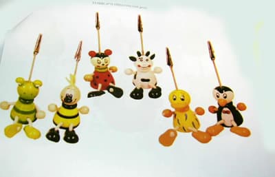 Pinza para notas de metal común (memoclip) sujeta a una figura de madera con forma de animal, policromada. Esta pinza metálica (de unos 3 cm aproximadamente) se sujeta a la figura mediante un vástago metálico, para mantener visible una nota, mensaje, foto, etc ...

Formas variadas (rana, pingüino, oso, etc ...). Alguna figura lleva cuerdas para hacer de brazos y patas rematadas en madera a guisa de manos y pies. 

Medidas de las figuras incluida la pinza entre 10 y 14 cm.