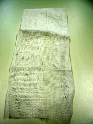 Compresa de tejido liso y poco tupido de ligamento tafetán blanqueado de 17 hilos de algodón 100%, de 24 g/m2, sin hilo de contraste azul (RX), sin esterilizar, de 15x26 cm, abierta, plegada sobre sí misma varias veces resultando una compresa de de 8 capas de 7,5x6 cm. El producto se presenta en cajas a granel pre contadas de 15.000 unidades en grupos separados por un papel entre sí de 5 unidades destinadas a ser esterilizadas y envasadas en sobres para la venta al pormenor de 5 á 10 unidades cada uno para uso quirúrgico