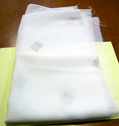Articulo consistente en un tejido de fibras sintéticas con un adorno bordado, presentado en rollos según pedido del cliente.
Uno de los bordes longitudinales del articulo está provisto de un cable de plomo que le da peso.  El borde opuesto tiene un orillo verdadero que evita el deshilachado.
La longitud del tejido que se corta del rollo corresponde a la anchura de la futura cortina. El tejido se transforma en una cortina de visillos siendo la parte inferior la parte del hilo de plomo ribeteado.
Se utiliza como cortina, pues está manifiestamente diseñado para transformarse en cortina.
Está hecho de fibras sintéticas discontinuas con un contenido superior al 85% en peso (100% poliéster).