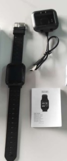 Artículo electrónico diseñado para llevarse en la muñeca como un reloj. Se presenta con esfera rectangular y pulsera de silicona con unas dimensiones aproximadas son: 120 x 34 x 11 mm.
Dispone de batería recargable de 90 mAh, pantalla TFT de 0,96” y conectividad Bluetooth. Sus funciones más relevantes son: 
•	Indicador de hora. Admite configuración manual de la hora, aunque necesita una configuración inicial con un teléfono móvil. 
•	Contador de pasos.
•	Monitorización del sueño.
•	Control de la frecuencia cardiaca. 
•	Recibir notificaciones y aviso de llamadas telefónicas. 
Este artículo no puede contestar llamadas, responder mensajes ni permite hablar a través suyo
Se presenta conjuntamente con un cargador USB.
Se utiliza fundamentalmente para indicar la hora, como podómetro y como aparato de comunicación.
