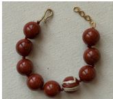 Artículo de adorno personal, pulsera hecha de bolitas de jaspe. Que van anudadas una auna con hilo. La pulsera dispone de un broche y de una cadena alargadora de latón macizo.
Se utiliza como objeto de adorno personal.
