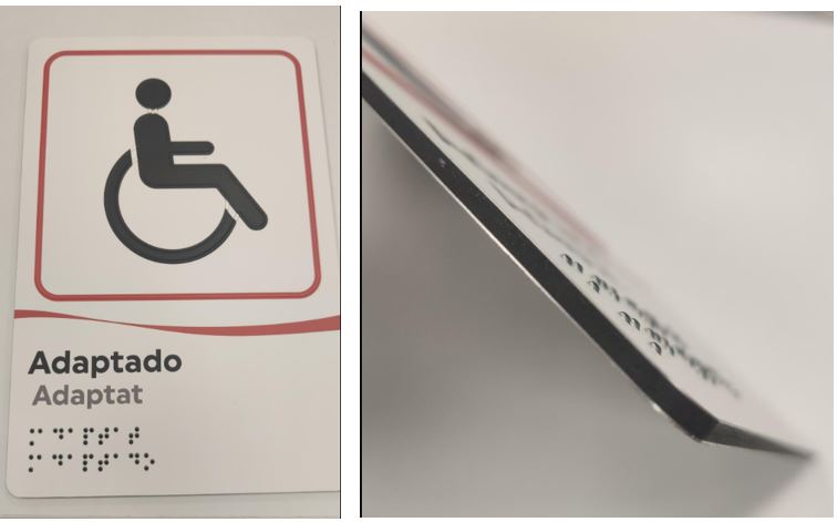Placa indicadora fabricada con un estratificado de aluminio+plástico+aluminio de 3 mm de espesor y forma rectangular. En la cara delantera incluye impresión de pictogramas por impresión digital, alto relieve y braille para personas con discapacidad visual. Véase la imagen aportada.