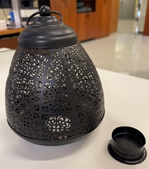 Se trata de un tipo de luminaria no eléctrica, en forma de farol fabricado en hierro con acabado en color negro mate. Tiene forma troncocónica y la estructura está calada con patrones ornamentales del tipo floral, lo que permite el paso de la luz, generando efectos decorativos. 
En la parte superior presenta un asa metálica para su transporte o suspensión, la base es circular y aloja un portavelas metálico extraíble con cierre giratorio, moldeado para colocar velas de té (tealight o velas calienteplatos). 
Dimensiones 14,00 cm de alto x 14,00 cm de ancho x 15,00 cm de base.
Función y uso:
El artículo está diseñado para introducir una vela de té y mediante la luz que emite resaltar su carácter decorativo.