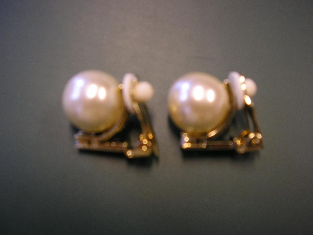 ARTICLE DE BIJOUTERIE FANTAISIE CONSISTANT EN UNE PAIRE DE BOUCLES D’OREILLE EN MÉTAL COMMUN DORÉ SUR UNE SOUS-COUCHE DE NICKEL ET COMPORTANT :
- UNE GROSSE PERLE D'IMITATION EN MATIÈRE PLASTIQUE RECOUVERTE D'UN PIGMENT À BASE D'OXYCHLORURE DE BISMUTH.
- UN PETIT BRILLANT D'IMITATION EN VERRE STRASS INCOLORE.

CES BOUCLES D’OREILLE SE FERMENT À L’AIDE D’UN CLIP PROTÉGÉ PAR UNE PETITE RONDELLE DE CAOUTCHOUC.