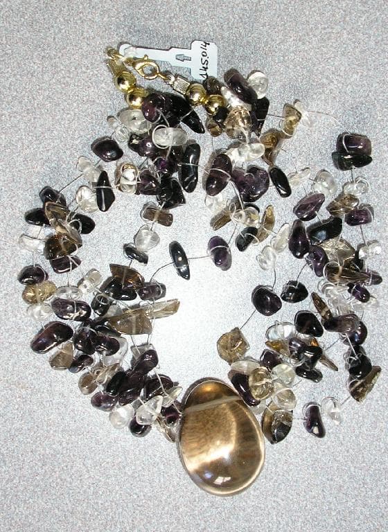 COLLIER COMPOSÉ DE CINQ RANGÉES PIERRES GEMMES (CRISTAL DE ROCHE ET CRISTAL FUMÉ) MONTÉES SUR DU FIL DE NYLON, AVEC UN PENDENTIF PRÉSENTANT LA FORME D'UN ŒUF ÉGALEMENT EN QUARTZ (NOM COMMERCIAL: CRISTAL FUMÉ).

L'ARTICLE COMPORTE UN FERMOIR EN MÉTAL DORÉ.