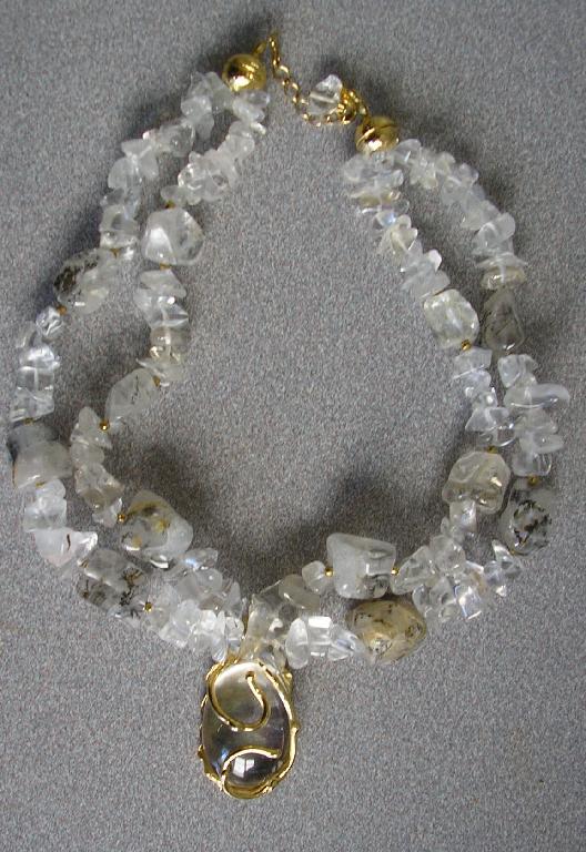 COLLIER COMPOSÉ DE DEUX RANGÉES PIERRES GEMMES (QUARTZ ET TOURMALINE) MONTÉES SUR DU FIL DE NYLON, AVEC UN PENDENTIF EN QUARTZ DE FORME OVALE MONTÉ SUR UN SUPPORT EN LAITON.

L'ARTICLE COMPORTE UN FERMOIR EN MÉTAL DORÉ.