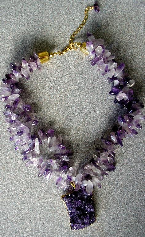 COLLIER RÉALISÉ EN PIERRES GEMMES (AMÉTHYSTE) MONTÉES SUR UN FIL EN NYLON, COMPORTANT DEUX RANGÉES, AVEC UN PENDENTIF COMPOSÉ D'UN MORCEAU DE QUARTZ BRUT.

L'ARTICLE PRÉSENTE UN FERMOIR EN MÉTAL DORÉ.