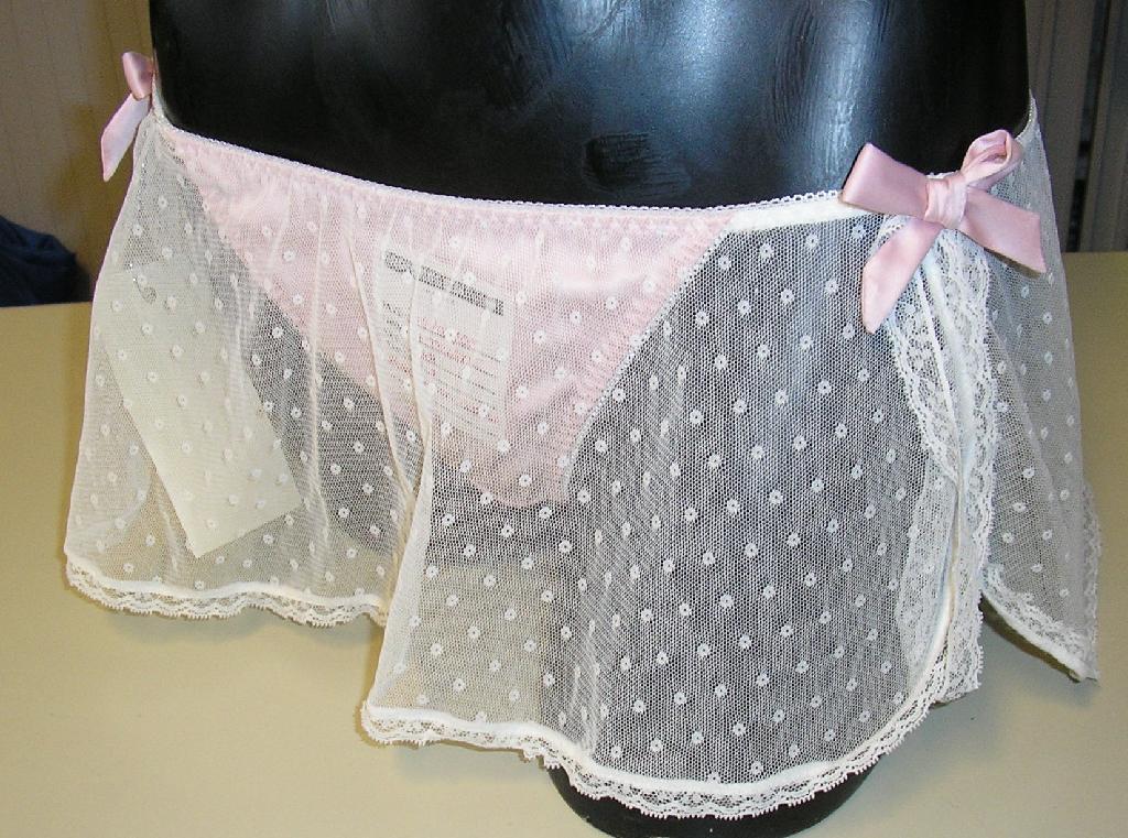 STRING CONFECTIONNÉ EN TISSU MAJORITAIREMENT DE FIBRES SYNTHÉTIQUES (71% POLYAMIDE - 26% POLYESTER - 3% ÉLASTHANE) ASPECT SATIN, AUX BORDURES POURVUES D'UN GALON ÉLASTIQUE.

L'ARTICLE COMPORTE UN VOLANT DE VOILE D'UNE LONGUEUR DE 16 CM, COUSU À LA TAILLE, BORDÉ D'UNE BANDE DE DENTELLE, FENDU SUR LES HANCHES.