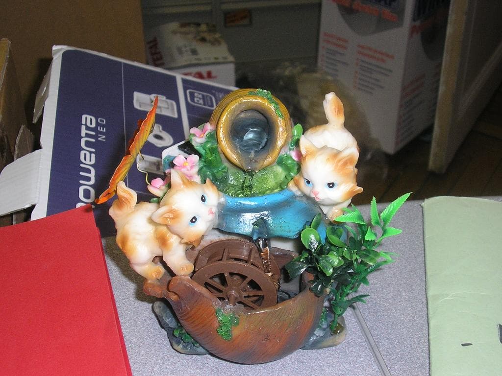 FONTAINE EN MATIERE PLASTIQUE (RESINE) AVEC DEUX PETITS CHATS ET UN PAPILLON EN METAL. CETTE FONTAINE FONCTIONNE AVEC UNE POMPE ET DEUX PILES. ELLE EST MUNIE D'UN INTERRUPTEUR. L'EAU COULE D'UNE JARRE ET GLISSE SUR LA ROUE ET STAGNE DANS UN POT.