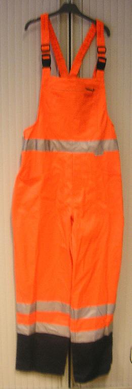 SALOPETTE OU COTTE À BRETELLES POUR HOMMES, EN TISSU DE COTON (60% COTON - 40% POLYESTER), TEINT DE COULEUR FLUORESCENTE, DE COUPE AMPLE, DESCENDANT JUSQU'AUX CHEVILLES.

CE VÊTEMENT COMPORTE DES BRETELLES ÉLASTIQUÉES S'ATTACHANT SUR L'AVANT PAR DEUX BOUCLES EN PLASTIQUE, UNE BAVETTE AVEC UNE POCHE PLAQUÉE AVEC FERMETURE À GLISSIÈRE, UNE TAILLE PARTIELLEMENT ÉLASTIQUÉE DANS LE DOS, UNE OUVERTURE D'AISANCE CÔTÉ DROIT SE FERMANT PAR DEUX BOUTONS, UNE OUVERTURE PARTIELLE AU NIVEAU DE L'ENTREJAMBE SE FERMANT GAUCHE SUR DROITE PAR DES BOUTONS ET DEUX POCHES PLAQUÉES SITUÉES AU NIVEAU DES HANCHES. 
L'EXTRÉMITÉ DES JAMBES EST CONFECTIONNÉE DANS UN TISSU DE COULEUR CONTRASTÉE.

ENFIN CE VÊTEMENT PRÉSENTE DES BANDES RÉTRORÉFLÉCHISSANTES À LA TAILLE AINSI QU'AUX JAMBES ET EST OURLÉ À L'EXTRÉMITÉ DES JAMBES.
