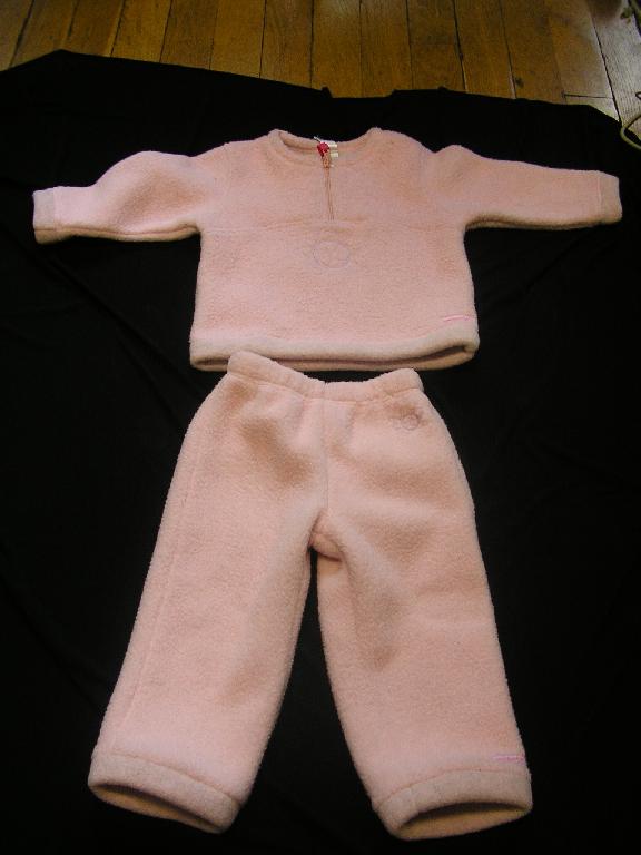ENSEMBLE POUR FILLETTE, EN BONNETERIE GRATTEE 100% POLYESTER, COMPOSE:
-D'UN VETEMENT DESTINE A RECOUVRIR LE HAUT DU CORPS, GENRE PULL, COMPORTANT UNE ENCOLURE ARRONDIE, UNE OUVERTURE PARTIELLE SUR LE DEVANT AU MILIEU AVEC UNE FERMETURE A GLISSIERE, DES MANCHES LONGUES AUX EXTREMITES OURLEES, LA BASE EST OURLEE, DECORATION BRODERIE EN FORME DE FLEUR SUR LE DEVANT ET LOGO PUBLICITAIRE COUSU AU BAS A GAUCHE DU VETEMENT.
-D'UN PANTALON, COMPORTANT UNE TAILLE ELASTIQUEE, LES EXTREMITES DES JAMBES SONT OURLEES, DECORATION BRODERIE EN FORME DE FLEUR EN HAUT A GAUCHE DU VETEMENT ET LOGO PUBLICITAIRE COUSU AU BAS DE LA JAMBE GAUCHE.