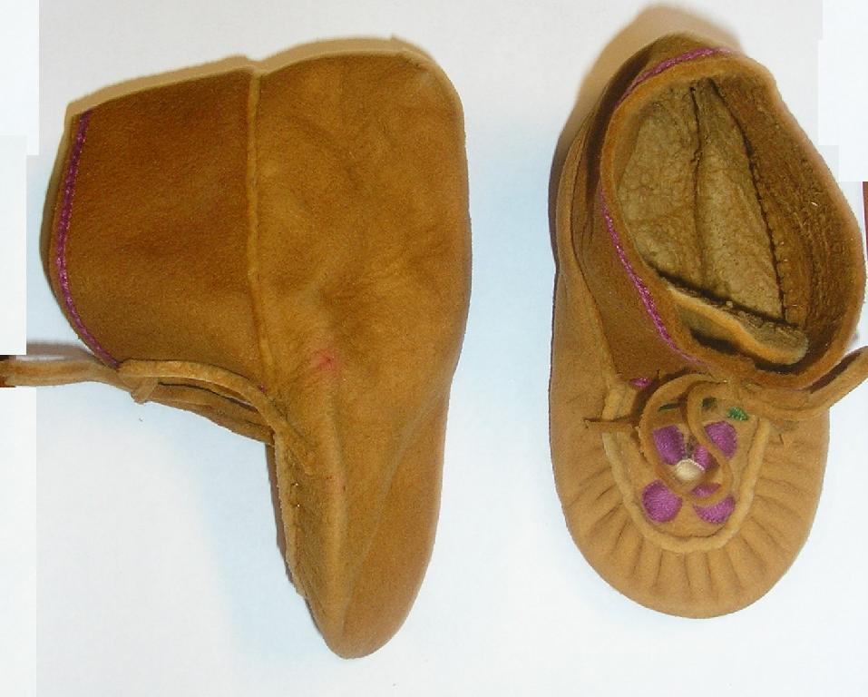 CHAUSSON POUR BÉBÉ RECOUVRANT LA CHEVILLE, À DESSUS ET SEMELLE EXTÉRIEURE EN CUIR RETOURNÉ, TYPE CHAUSSURE D'INDIEN, AVEC UNE SEMELLE EXTÉRIEURE RAPPORTÉE PAR COUTURE.

IL PRÉSENTE SUR LE DESSUS UNE LANGUETTE AINSI QU'UNE FERMETURE AU MOYEN DE LIENS EN CUIR À NOUER.