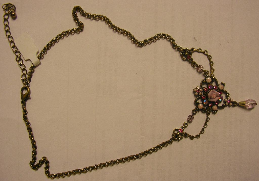 ARTICLE DE BIJOUTERIE FANTAISIE CONSISTANT EN UN COLLIER EN MÉTAL COMMUN (35% FER BLANC, 62% PLOMB ET 3% ANTIMOINE) DE COULEUR BRONZE, COMPORTANT:
 -UNE ROSE EN PORCELAINE ROSE 
 -DES STRASS EN CRISTAUX DE VERRE
 -DES PARTIES EN VERRE

LONGUEUR DE LA CHAINE: 48.5 CM
DIMENSIONS DE LA DÉCORATION: 7.5 X 4 X 0.7 CM