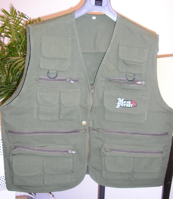 AUTRE VÊTEMENT POUR HOMMES, GENRE GILET, CONFECTIONNÉ EN TISSU DE COTON (100% COTON), DESCENDANT SOUS LES HANCHES, SANS MANCHE, AVEC UNE DOUBLURE PARTIELLE, AVEC UNE ENCOLURE EN V, AVEC UNE OUVERTURE COMPLETE SUR LE DEVANT SE FERMANT A L’AIDE D'UNE FERMETURE À GLISSIÈRE ET D’UNE PETITE PATTE DE BOUTONNAGE SE FERMANT GAUCHE SUR DROITE PAR BOUTON-PRESSION, AVEC UN BIAIS SUR LE POURTOUR DU VETEMENT, AVEC UN LOGO PUBLICITAIRE BRODE SUR UNE POCHE.

CE VETEMENT COMPORTE :

-AU DESSOUS DES EPAULES DEUX POCHES MUNIES D’UN RABAT DE PROTECTION SE FERMANT PAR VELCRO A LA BASE UNE GANSE ET UN ANNEAU EN MATIERE PLASTIQUE, AU NIVEAU DE LA POITRINE DEUX POCHES SE FERMANT A L’AIDE D’UNE FERMETURE A GLISSIERE, DEUX PETITES POCHES ET UNE GRANDE POCHE MUNIES CHACUNE D’UN RABAT DE PROTECTION SE FERMANT PAR VELCRO, AU NIVEAU DE LA TAILLE DEUX POCHES SE FERMANT A L’AIDE D’UNE FERMETURE A GLISSIERE, AU NIVEAU DES HANCHES UNE GRANDE POCHE SE FERMANT A L’AIDE D’UNE FERMETURE A GLISSIERE ET SUPERPOSEES DEUX PETITES POCHES MUNIES D'UN RABAT DE PROTECTION SE FERMANT PAR VELCRO, DANS LE DOS UNE GRANDE POCHE GIBECIERE SE FERMANT A L’AIDE D’UNE FERMETURE A GLISSIERE, AVEC UNE POCHE INTERNE SE FERMANT PAR UNE FERMETURE A GLISSIERE.
POIDS: 480 GRAMMES. 
TAILLE : XL.