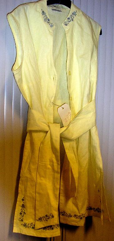 BLOUSE POUR FEMMES DESCENDANT JUSQU’AU DESSUS DE LA MI-CUISSE, EN TISSU DE LIN (55 %) ET DE COTON (45 %), SANS MANCHES, AVEC UN PETIT COL DROIT, UNE OUVERTURE COMPLETE SUR LE DEVANT SE FERMANT COTE DROIT SUR GAUCHE PAR BOUTONS, DEUX FENTES LATERALES D’ENVIRON 24 CM ET DES BRODERIES SUR LE COL ET A LA BASE.
CETTE ARTICLE EST PRESENTE AVEC UNE CEINTURE DE MEME MATIERE TEXTILE, COMPOSITION, COULEUR ET COMPORTANT LA MEME BRODERIE.

LONGUEUR BASE DU COL – BASE DU VETEMENT POUR UNE TAILLE 44 : 82 CM