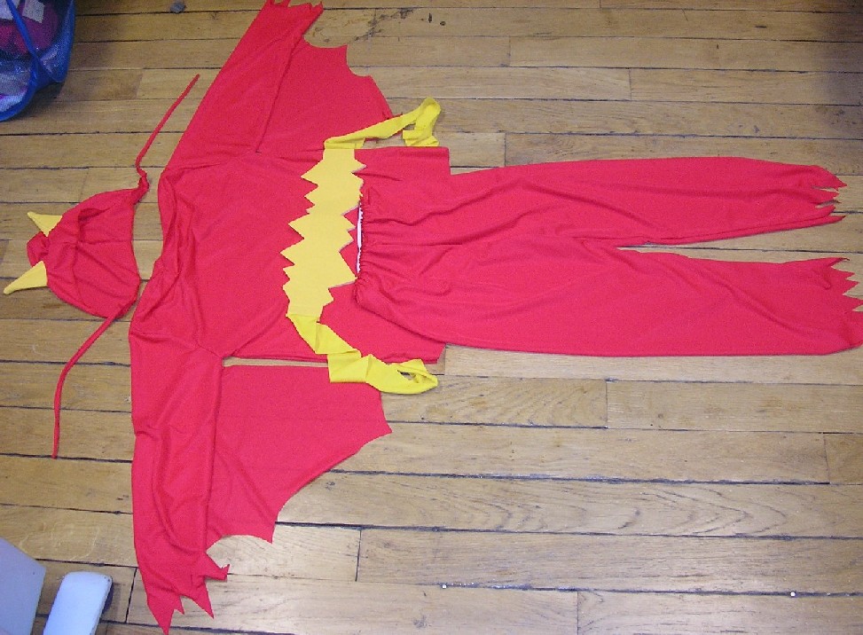 DÉGUISEMENT POUR ENFANTS EN ÉTOFFE DE BONNETERIE DE FIBRES SYNTHÉTIQUES (POLYESTER) REPRÉSENTANT UN DIABLOTIN.
CET ARTICLE COMPREND PLUSIEURS ÉLÉMENTS:
   - UN ENSEMBLE, RÉALISÉ DANS LA MÊME ÉTOFFE DE COULEUR UNIE, COMPOSÉ D'UN VÊTEMENT DESTINÉ À RECOUVRIR LA PARTIE SUPÉRIEURE DU CORPS, DU GENRE BLOUSE, ET D'UN PANTALON ÉLASTIQUÉ À LA TAILLE. 
LA BLOUSE EST MUNIE D'AILERONS COUSUS SOUS LES MANCHES ET D' UNE OUVERTURE PARTIELLE DANS LE DOS AU NIVEAU DU COL FERMÉE AU MOYEN DE VELCRO.
LE BAS DES MANCHES ET DU PANTALON SONT DÉCOUPÉS EN FORME DE POINTES.
   - UNE CEINTURE DE COULEUR CONTRASTÉE, SE NOUANT DANS LE DOS, DÉCOUPÉE EN FORME DE POINTES SUR LE DEVANT.
   - UNE CAGOULE DE LA MÊME ÉTOFFE QUE LE VÊTEMENT MUNIE DE DEUX EMPIÈCEMENTS TEXTILES EN FORME DE CORNE, DE LA MÊME ÉTOFFE QUE LA CEINTURE, ET DE DEUX LIENS PERMETTANT DE NOUER L'ARTICLE AU NIVEAU DU COU.