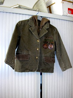 VETEMENT DESTINE A RECOUVRIR LA PARTIE SUPERIEURE DU CORPS, GENRE VESTE, POUR GARÇON, EN TISSU 100% COTON, COMPOSE DE DEUX PANNEAUX FRONTAUX ET DORSAUX, DE MANCHES LONGUES DONT LES EXTREMITES SONT OURLEES, AVEC DES BOUTONS ET UN RENFORT AUX COUDES, D'UN COL TAILLEUR, D'UNE OUVERTURE COMPLETE SUR LE DEVANT, AU MILIEU, AVEC DES BOUTONS SE FERMANT DE GAUCHE SUR DROITE, D'UNE PETITE POCHE POITRINE COTE GAUCHE, AVEC FERMETURE A GLISSIERE ET DES MEDAILLES SUSPENDUES A DES ATTACHES, D'UNE POCHE AVEC RABAT DE CHAQUE COTE DU VETEMENT, SOUS LA TAILLE, LA BASE DU VETEMENT EST OURLEE, AVEC UNE IMPRESSION AU DOS DU VETEMENT. 
CET ARTICLE COMPORTE UN ACCESSOIRE DU VETEMENT EN ETOFFE DE BONNETERIE DE COTON, AMOVIBLE, CONSTITUANT UN PLASTRON-CAPUCHE AVEC FERMETURE A GLISSIERE, S'ATTACHANT SUR LE DEVANT DE LA VESTE A L'INTERIEUR PAR BOUTONS-PRESSIONS.