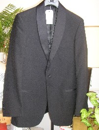 COSTUME POUR HOMMES, SOUS FORME DE SMOKING, CONSTITUÉ DE DEUX PIÈCES CONFECTIONNÉES DANS LE MÊME TISSU DE FIBRES SYNTHÉTIQUES (100% POLYESTER), UNI DE COULEUR NOIRE COMPOSE :

- D'UNE VESTE DONT L'EXTÉRIEUR EST CONFECTIONNE DE QUATRE PANNEAUX DORSAUX ET DEUX PANNEAUX FRONTAUX COUSUS ENSEMBLES DANS LE SENS DE LA LONGUEUR, DESCENDANT SUR LES HANCHES, AVEC UN COL CHALE RECOUVERT DE SATIN, AVEC DES MANCHES LONGUES DÉCORÉES DE QUATRE BOUTONS EN SATIN ET COMPORTANTUN OURLET À LEUR EXTRÉMITÉ, AVEC UNE OUVERTURE COMPLÈTE SUR LE DEVANT SE FERMANT GAUCHE SUR DROITE PAR UN BOUTON EN SATIN, AVEC UNE POCHE POITRINE SUR LE CÔTÉ GAUCHE, AVEC DEUX POCHES HORIZONTALES SOUS LA TAILLE DOTEES DE PETITS PARMENTS EN SATIN, AVEC DEUX POCHES INTERNES, AVEC UNE DOUBLURE COMPLETE EN TISSU SATINE, AVEC UN OURLET A LA BASE.

- D'UN PANTALON DESCENDANT JUSQU'AUX CHEVILLES, AVEC SIX PASSANTS A LA CEINTURE, AVEC UNE OUVERTURE PARTIELLE SUR LE DEVANT SE FERMANT GAUCHE SUR DROITE A L’AIDE D’UN BOUTON ET D’UNE FERMETURE À GLISSIÈRE DISSIMULEE SOUS UNE PATTE DE PROTECTION, AVEC DEUX POCHES LATÉRALES SUR LE DEVANT AU NIVEAU DES HANCHES ET DEUX POCHES ARRIÈRES SE FERMANT PAR UN BOUTON, AVEC UN GALON EN TISSU SATINÉ COUSU SUR LA COUTURE LE LONG DE LA JAMBE, AVEC UN SURFILAGE A LA BASE.

TOUS LES COMPOSANTS DU COSTUME SONT DE MÊME STRUCTURE, DE MÊME COULEUR, DE MÊME COMPOSITION ET DE TAILLES CORRESPONDANTES. LES DEUX PIÈCES SONT CONDITIONNÉES ENSEMBLE POUR LA VENTE AU DÉTAIL.